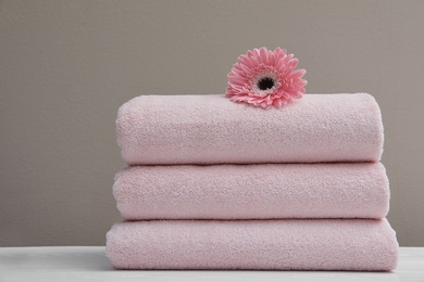 Photo of Stack of fresh towels with flower on table