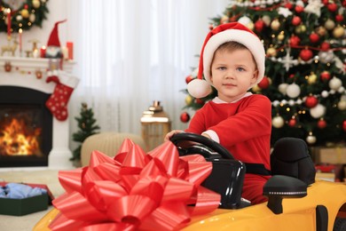 Cute little boy driving toy car in room decorated for Christmas