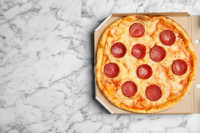 Photo of Tasty pepperoni pizza in cardboard box on white marble table, top view. Space for text