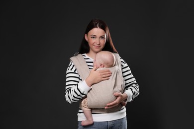 Mother holding her child in baby carrier on black background