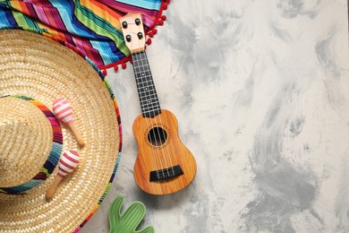 Photo of Mexican sombrero hat, guitar, maracas and colorful poncho on grey textured background, flat lay. Space for text