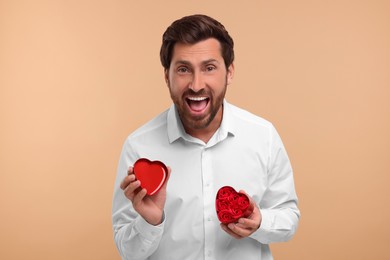 Photo of Emotional man holding decorative heart shaped box with roses on beige background