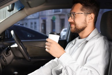 Photo of Coffee to go. Handsome man with paper cup of drink in car, space for text