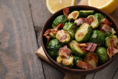 Photo of Delicious roasted Brussels sprouts and bacon in bowl on wooden table, closeup