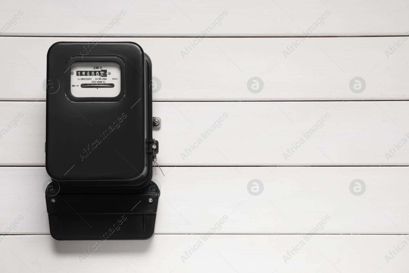 Photo of Electricity meter on white wooden wall, space for text