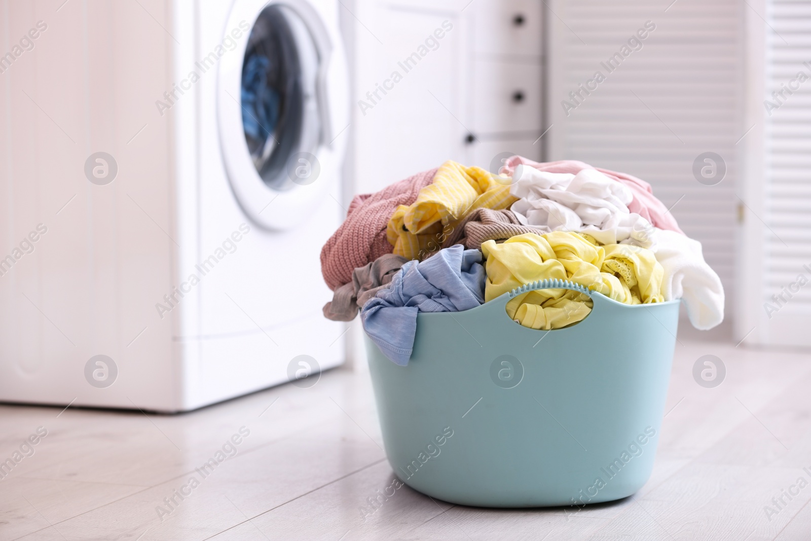 Photo of Light blue basket with dirty laundry on floor indoors, space for text