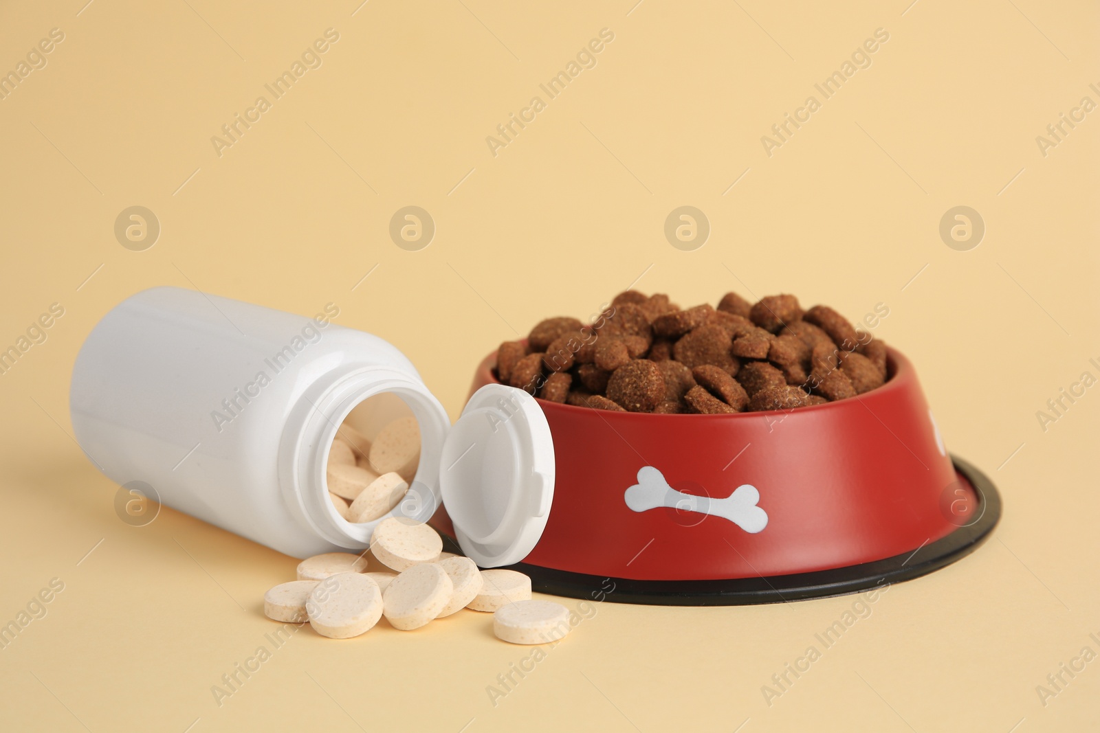 Photo of Bottle with vitamins and dry pet food in bowl on beige background