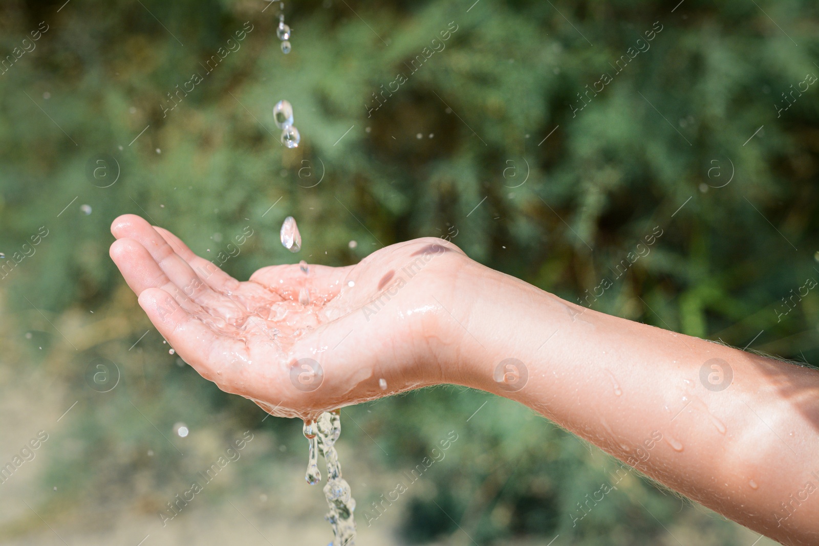 Photo of Pouring water into kid`s hand outdoors, closeup