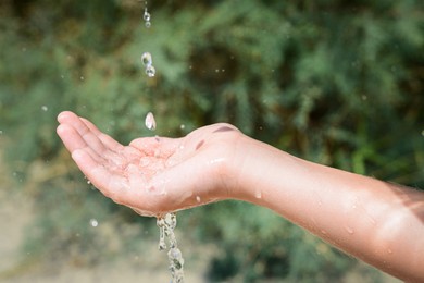 Photo of Pouring water into kid`s hand outdoors, closeup