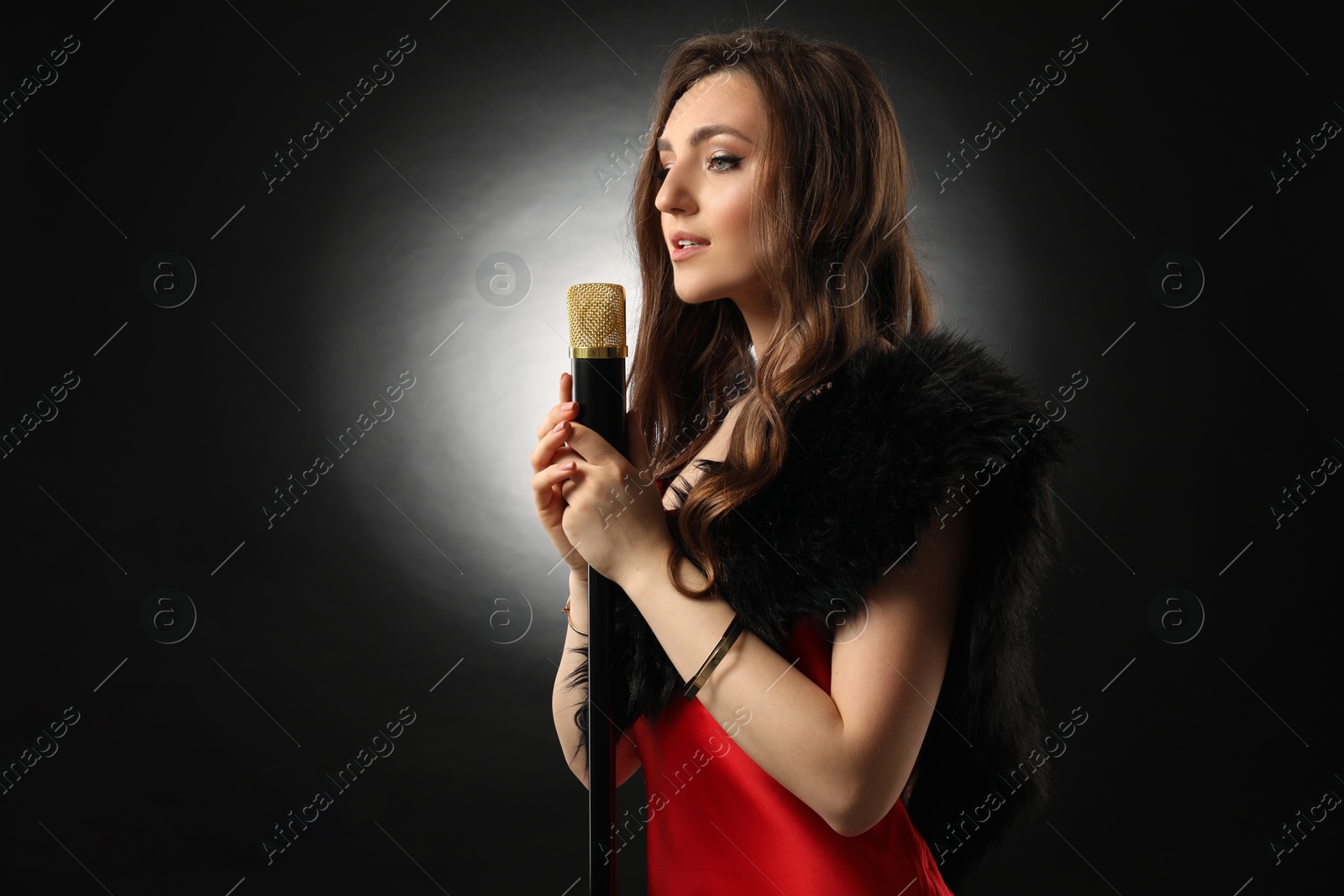 Photo of Beautiful young woman with microphone singing on black background