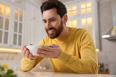 Photo of Man enjoying delicious soup at light table in kitchen