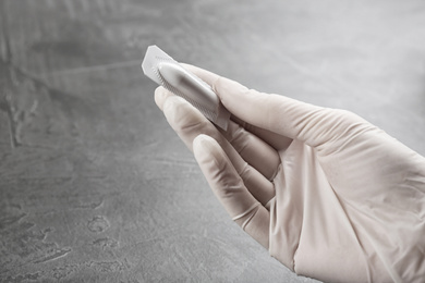 Photo of Woman holding suppository at grey table, closeup. Hemorrhoid treatment