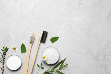 Bamboo toothbrushes, flowers and herbs on light grey table, flat lay. Space for text