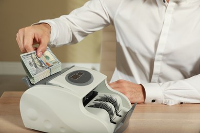 Man putting money into banknote counter at wooden table indoors, closeup