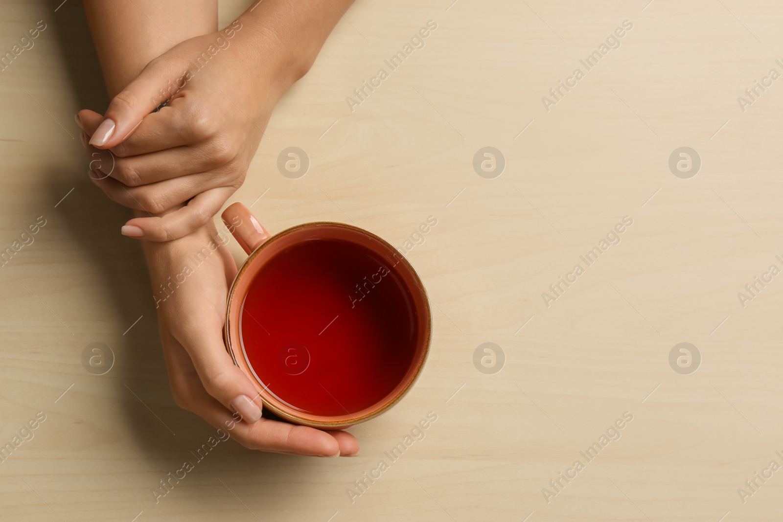 Photo of Woman holding cup of tea at wooden table, top view. Space for text