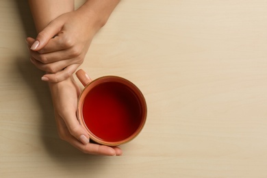 Woman holding cup of tea at wooden table, top view. Space for text