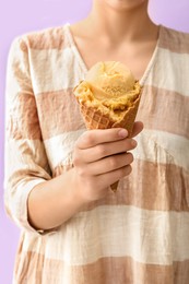 Woman holding yellow ice cream in wafer cone on violet background, closeup