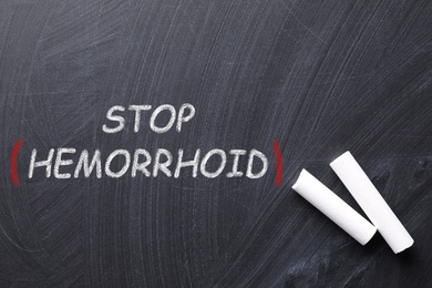 Image of Pieces of white chalk and phrase Stop Hemorrhoid on blackboard, flat lay