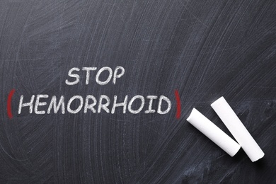 Pieces of white chalk and phrase Stop Hemorrhoid on blackboard, flat lay