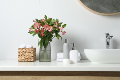 Photo of Vase with beautiful Alstroemeria flowers and toiletries near sink in bathroom