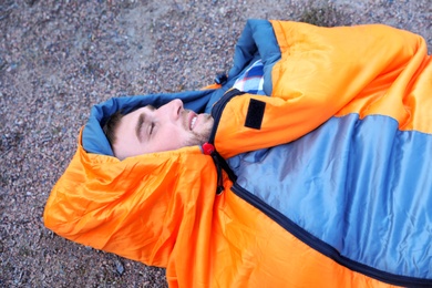 Male camper lying in sleeping bag on ground, view from above