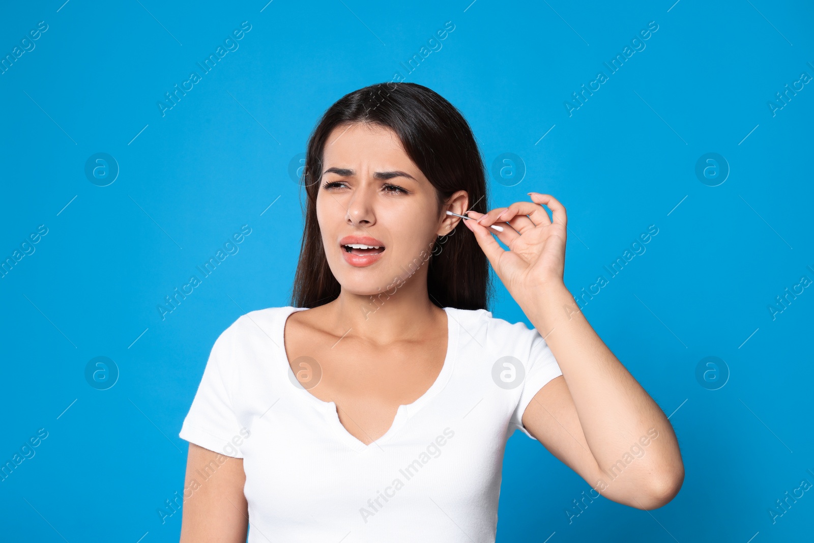 Photo of Young woman cleaning ear with cotton swab on light blue background