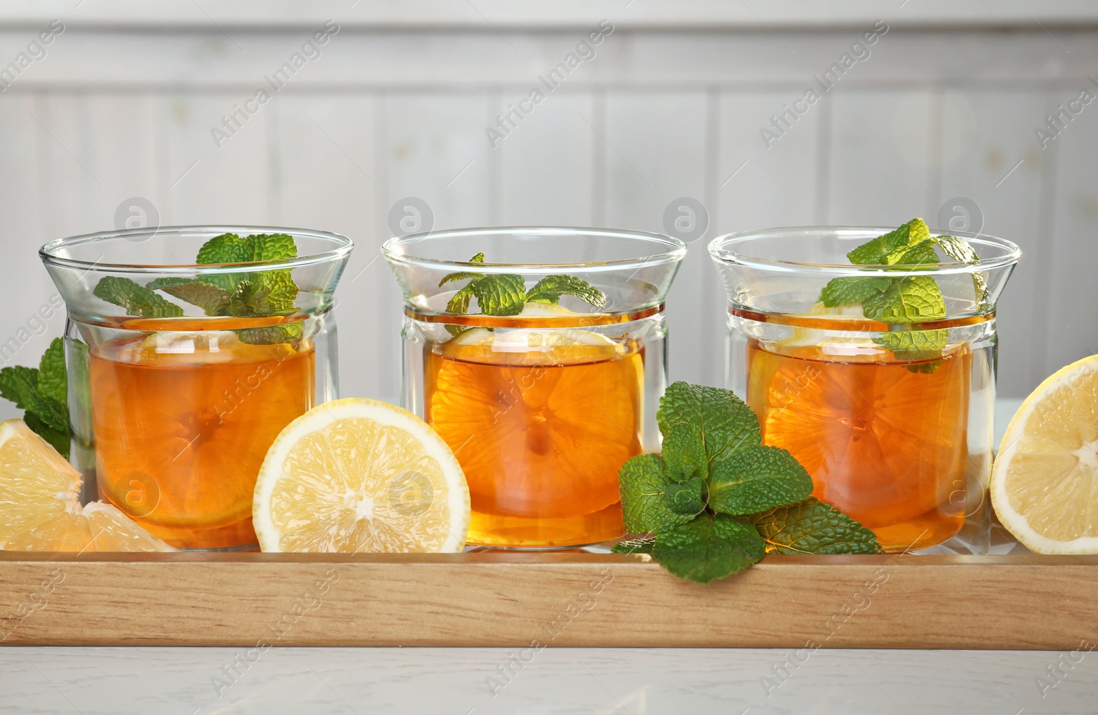 Photo of Wooden tray with hot tea in glasses on table, closeup