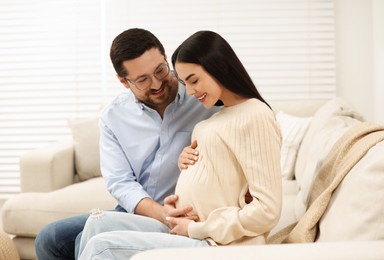 Photo of Happy pregnant woman spending time with her husband on sofa at home