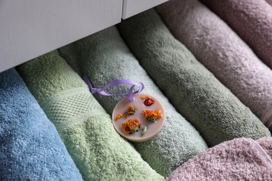 Photo of Beautiful scented wax sachet in dresser drawer with colorful towels, closeup