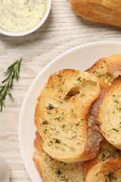 Tasty baguette with garlic, rosemary, dill and oil on white wooden table, flat lay