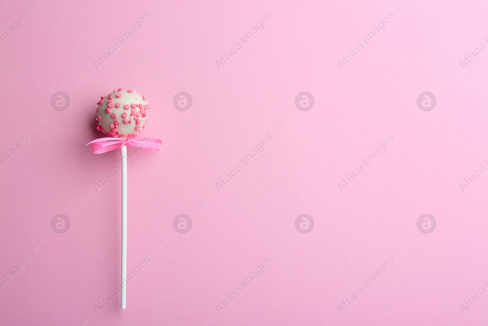 Photo of Tasty cake pop with bow on light pink background, top view. Space for text