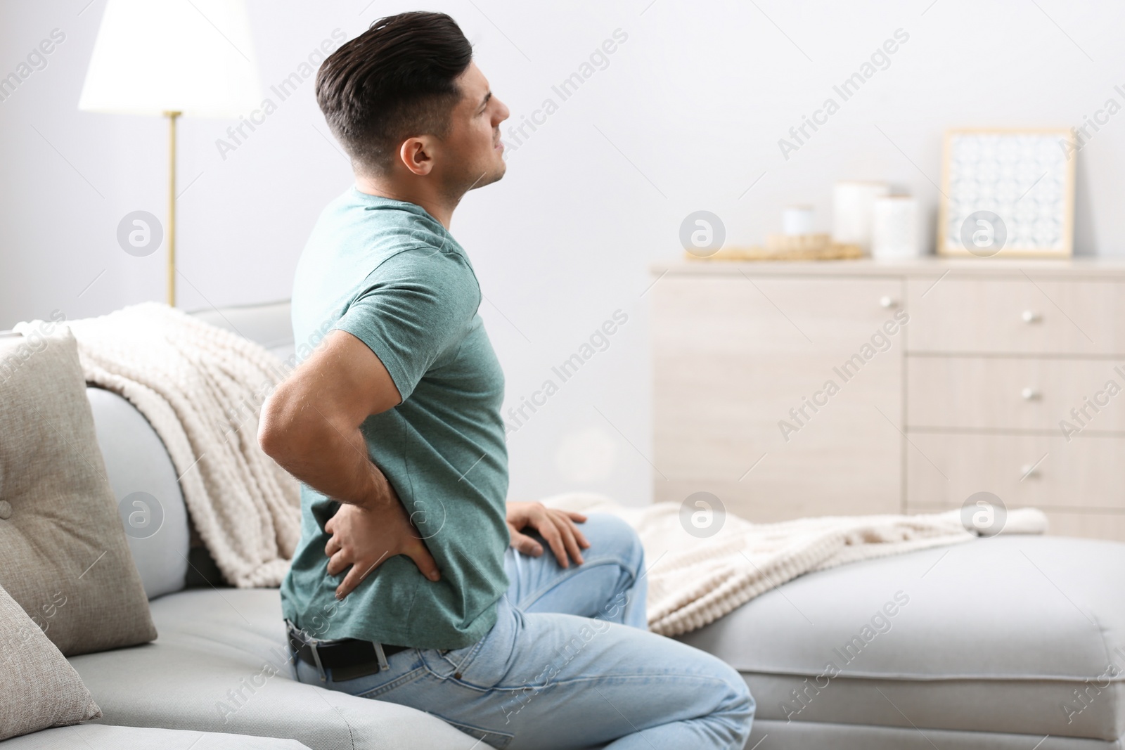 Photo of Man suffering from back pain at home. Bad posture problem