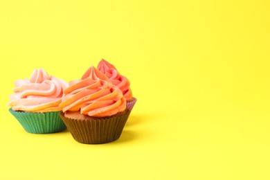 Photo of Delicious cupcakes with bright cream on yellow background. Space for text