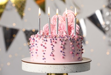Photo of Beautifully decorated birthday cake on stand against blurred festive lights