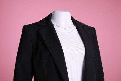Photo of Female mannequin with necklace dressed in black classic jacket and white t-shirt on pink background