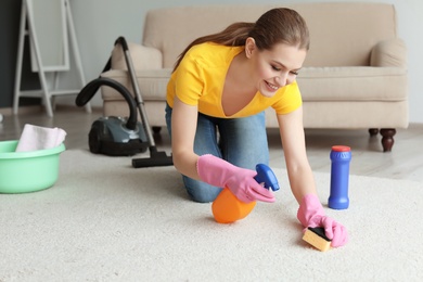 Photo of Young woman cleaning carpet at home