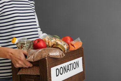 Photo of Woman holding donation box with food on gray background, closeup