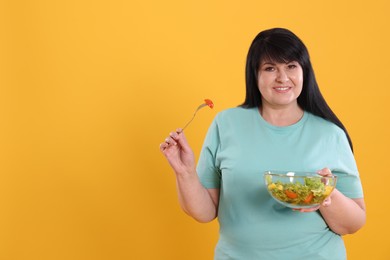 Photo of Beautiful overweight woman eating salad on yellow background, space for text. Healthy diet