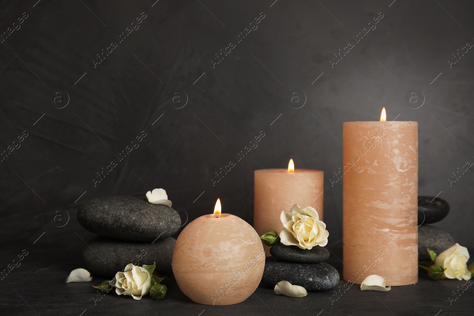 Photo of Burning candles, spa stones and flowers on dark grey table, space for text