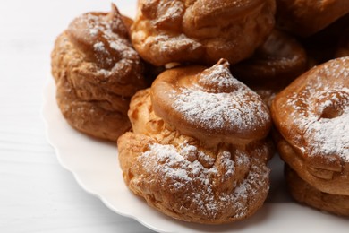 Photo of Delicious profiteroles with powdered sugar on white table, closeup
