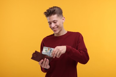 Photo of Happy man putting money into wallet on yellow background