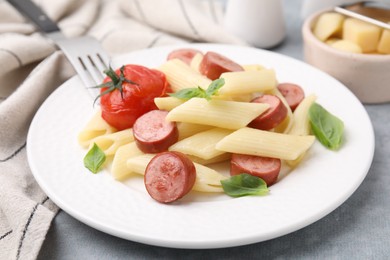 Tasty pasta with smoked sausage, tomato and basil on light grey table, closeup