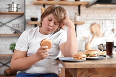 Photo of Overweight boy at table with fast food in kitchen