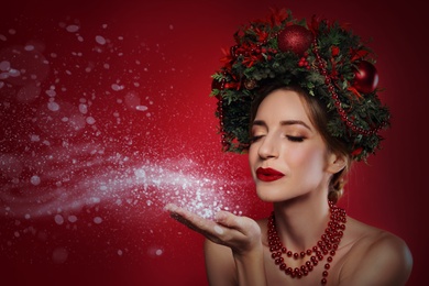 Image of Beautiful young woman with Christmas wreath blowing kiss on red background