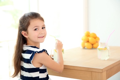 Photo of Little girl with natural lemonade at table indoors