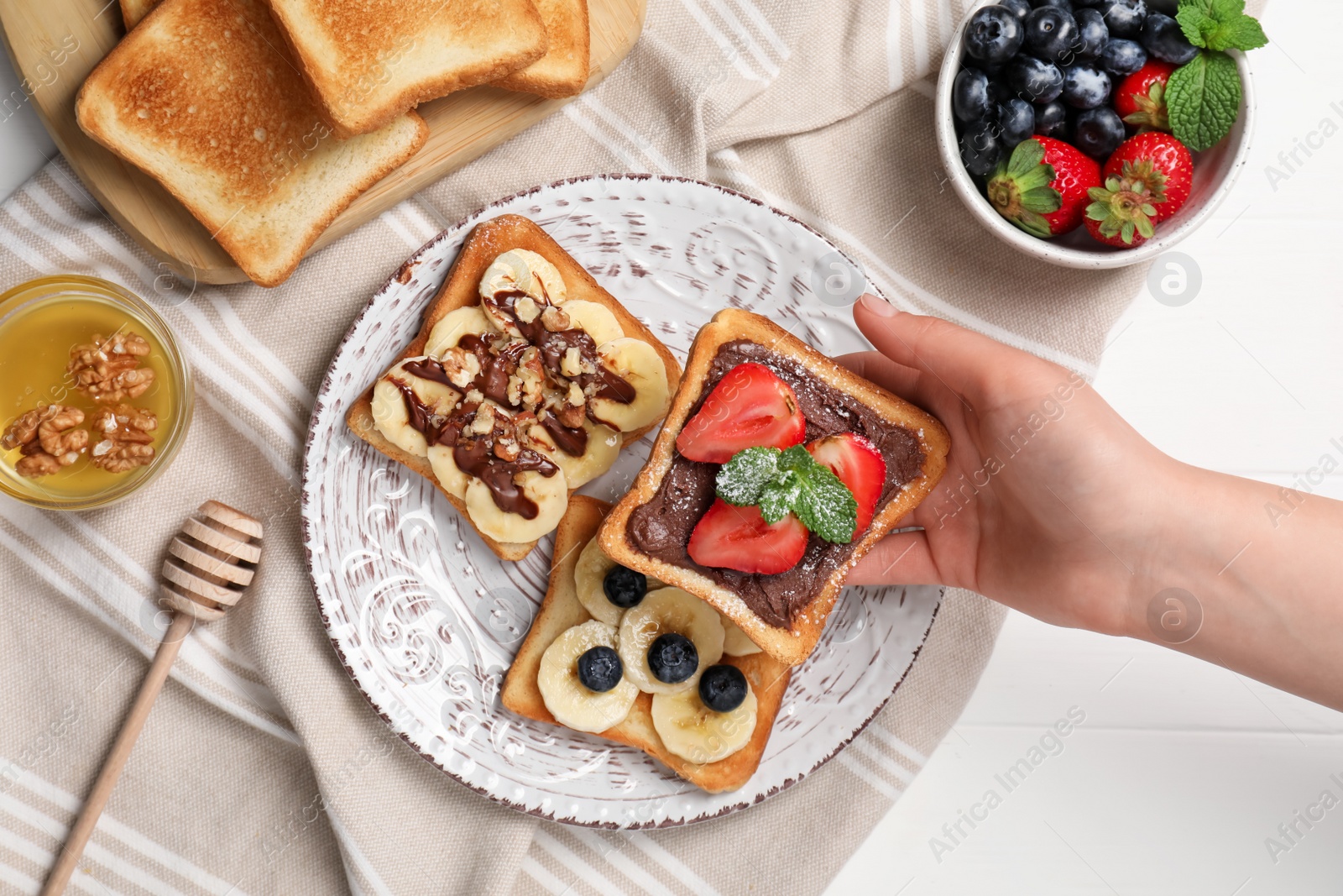 Photo of Woman holding delicious sweet toast at white wooden table, top view