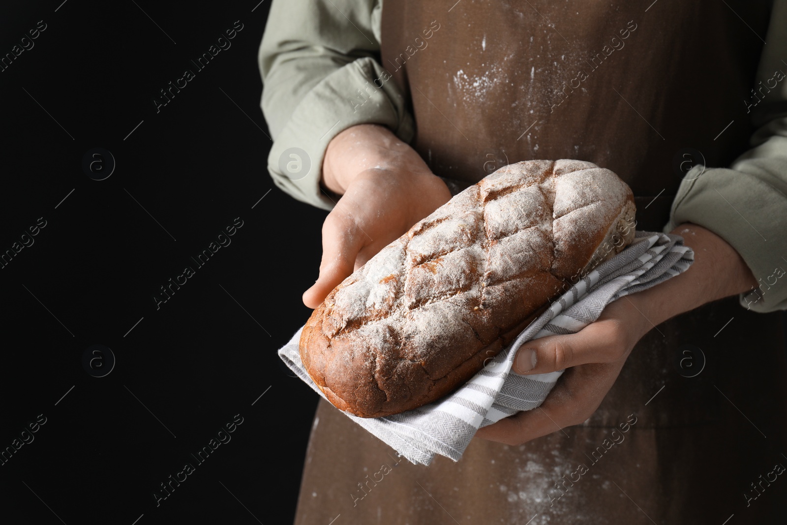 Photo of Woman holding freshly baked bread on black background, closeup. Space for text