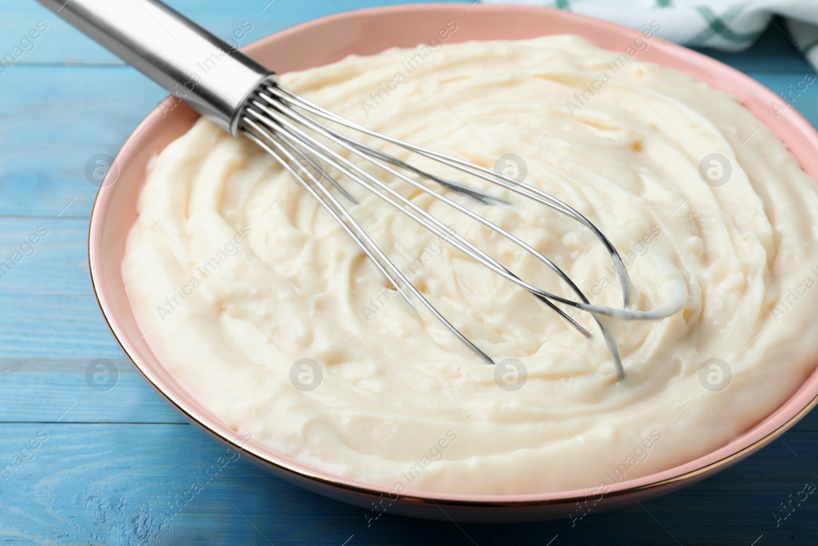 Photo of Pastry cream with balloon whisk on light blue wooden table, closeup