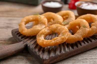 Photo of Wooden board with fried onion rings on table, closeup