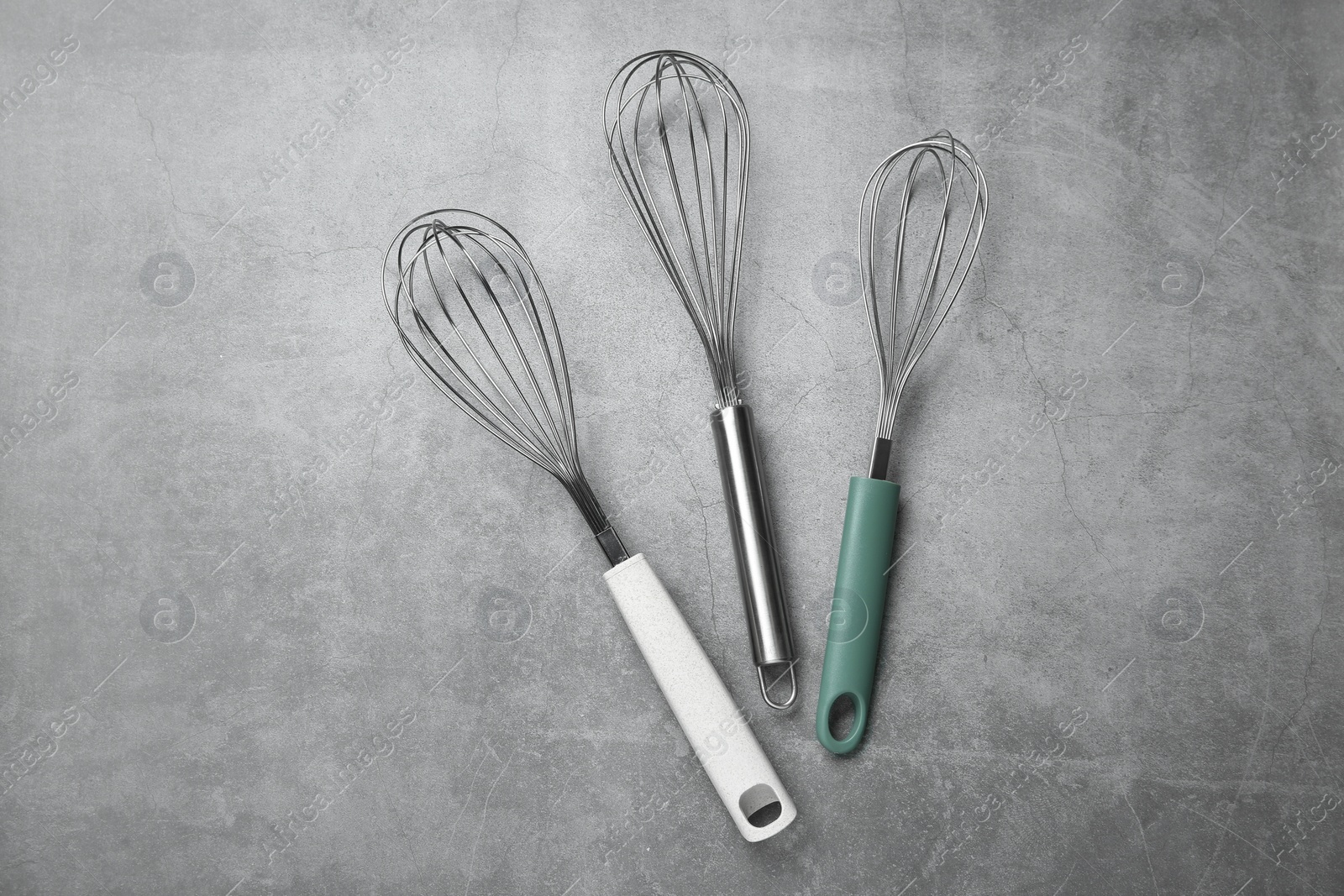 Photo of Metal whisks on gray table, top view